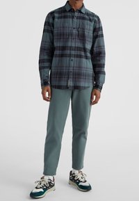 Hemdenhemd mit einem karomuster in Türkis und Dunkel, kombiniert mit helltürkisen Hosen und schwarzen, grünen und weißen Turnschuhen.