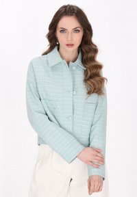 Jachetă texturată de culoare albastru deschis, cu formă pătrată, închidere frontală cu buton și două buzunare pe piept, concepută cu un model subtil în carouri.
