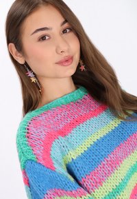Maglione a maglia con strisce rosa, blu, verde e lavanda; presenta un collo ampio e un filato testurizzato. Orecchini a forma di stella multicolore pendenti.