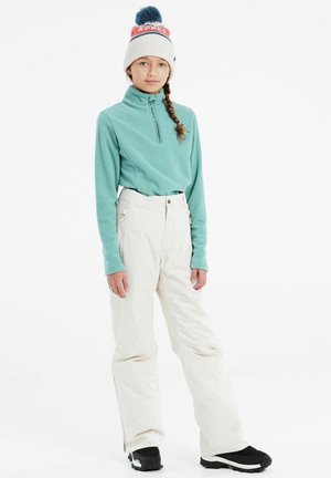 Licht teal fleecetop met halve ritssluiting, off-white skibroek met ritszakken en zwarte laarzen. Warme muts met rode en blauwe accenten.