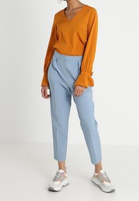 Pitkähihaista, V-kaula-aukkoista paitaa kirkkaan oranssina; yhdistetty vaaleansinisiin räätälöityihin housuihin. Urheilulliset valkoiset lenkkarit monivärisin tehostein.