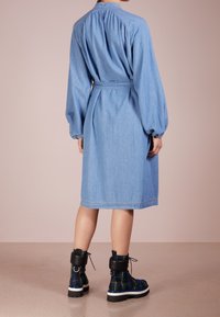 Ljusblå denimskjortklänning med långa puffärmar, cinchad midja och knälång fåll, parat med svarta och rutiga ankelskor.