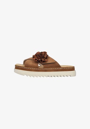 Tan leather slide sandals with a decorative brown flower on the strap, textured footbed, and chunky white serrated sole.