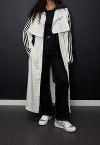 Lång vit kappa med svarta detaljer, kombinerad med svarta högmidjade byxor. Sportiga sneakers med färgdetaljer. Snygg design, avslappnad passform.