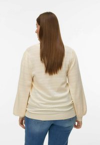 Pull crème clair avec un motif en maille ajourée texturée, manches longues bouffantes et bas ajusté. Assorti à un jean en denim bleu.