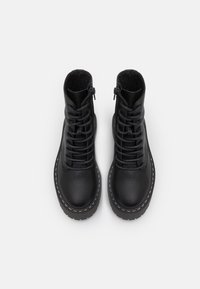 Bottines en cuir noir avec finition texturée, design à lacets, fermeture éclair, et semelles en caoutchouc avec détails de couture blanche.
