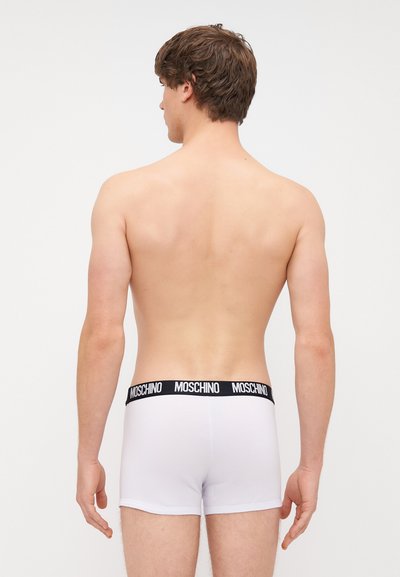 Biele boxerky s čiernym elastickým pásom Moschino, s hladkým povrchom a priliehavým strihom, z pohľadu zozadu.