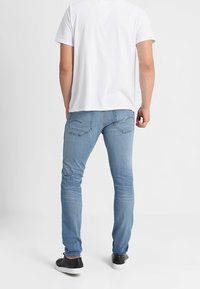 Vaqueros de mezclilla azul claro con un corte ajustado, que presentan bolsillos traseros con costuras sutiles. Combinados con una camiseta blanca lisa y zapatillas negras.