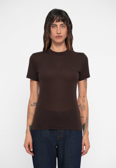 T-shirt marron à manches courtes en coton avec un col rond. Présente une texture lisse et une coupe ajustée. Porté avec un jean bleu.