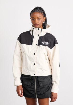 White and black half-zip jacket with hood, featuring snap buttons and logo on chest; smooth texture with a relaxed, cropped fit.