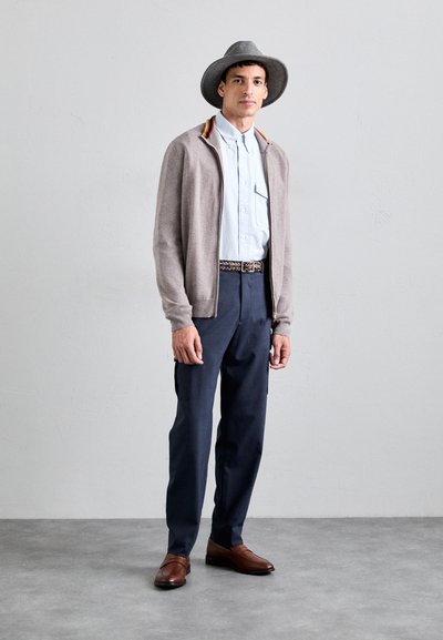 Cárdigan gris claro con detalles de cuello colorido, camisa azul de botones, pantalones cargo azul marino y mocasines marrones, complementados con un sombrero gris.
