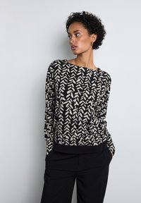 Schwarzer Pullover mit weißem abstraktem Blättermuster, runder Ausschnitt, langen Ärmeln und schwarzem Taillenbund. Glatte Textur, lässiges Design.