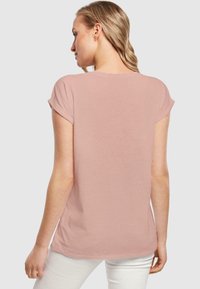 Kortermet rosa t-skjorte med en jevn tekstur, avslappet passform og rullede mansjetter, med rund hals og en lett svai bak.