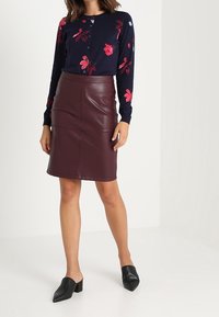 Marinblå blommig cardigan med långa ärmar och knappar, kombinerad med en figurnära burgundy läderkjol och svarta öppna-tofflor.