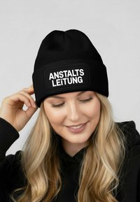 Black knit beanie with a wide band featuring the white text "ANSTALTSLEITUNG" against a solid background. Smooth texture, fitted design.