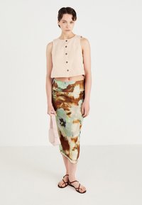 Crème cropped tanktop met knoopsluiting, gecombineerd met een kleurrijke, vloeiende midi-rok met bloemen in groen- en bruine tinten. Geaccessoiresd met een roze tas.