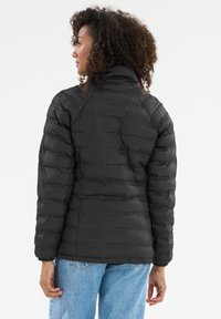 Sort dunjakke med vandret quiltet design, høj krave og glat tekstur. Kombineret med lyseblå jeans. Set bagfra.