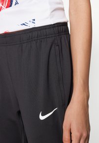 Sorte treningsbukser med elastisk midje og to sidelommer. Har en hvit Nike-logo på venstre side. Glatt tekstur.