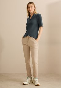 Tmavě modrý polo triko s krátkým rukávem, v kombinaci se béžovými zúženými kalhotami s kapsami a stahovací šňůrkou. Bílá a mátová sportovní obuv dotváří celkový vzhled.