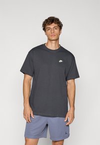 Grå bomulds T-shirt med korte ærmer, der har et lille hvidt Nike-logo på brystet. Kombineret med lyse lilla træningsshorts.