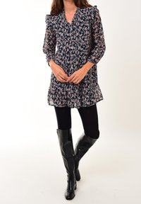 Vestido negro con estampado floral, de manga larga, escote en forma de V y dobladillo con volantes; combinado con botas negras hasta la rodilla sobre pantys opacos negros.