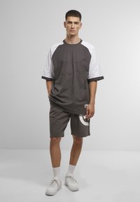 Grijze en witte sportshirt met korte mouwen in combinatie met bijpassende grijze shorts met een grote grafische print. Footwear is witte sneakers.
