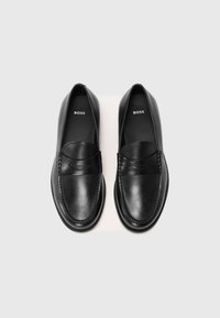 Zwarte leren loafers met een gladde afwerking, instapontwerp en decoratieve stikdetails over de wreef. "BOSS" branding zichtbaar aan de binnenkant.