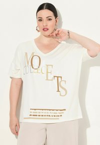 Hvid, kortærmet V-hals T-shirt med guld- og sølvtekst, der siger "MOMENTS NOT THINGS." Blødt stof med en afslappet pasform.