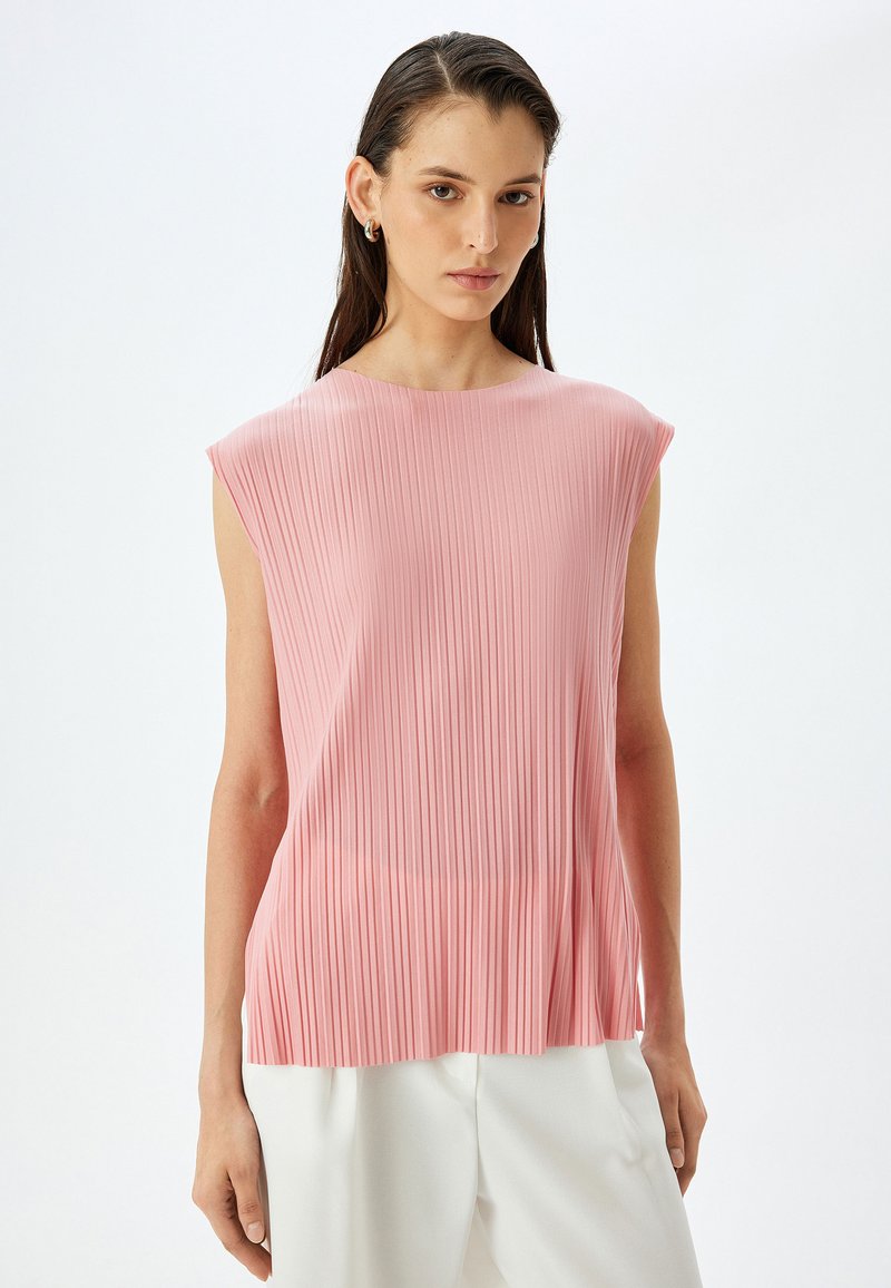 Rosa plissierte ärmellose Bluse mit rundem Ausschnitt, glatter Textur und fließender Silhouette, kombiniert mit weißen Hosen.