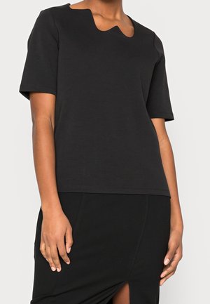 Czarny top z krótkim rękawem wykonany z miękkiej tkaniny, z falującym dekoltem i prostym krojem. Dopasowany do czarnej spódnicy z bocznym rozcięciem.