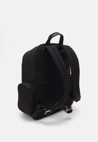 Mochila de tela negra con respaldo de malla acolchada, correas ajustables y un bolsillo lateral. Diseño elegante y aerodinámico con un acento brillante.