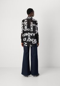 Svart-hvitt langermet skjorte med overlappende DKNY-logo mønster, kombinert med vide mørke denimbukser. Enkelt, elegant design.