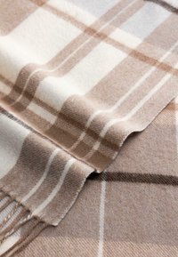 Soft wool scarf with beige and white plaid pattern, folded to show fringed ends and textured fabric close-up.