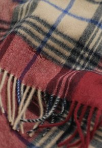 Écharpe en laine douce avec un motif écossais rouge, crème, noir et bleu et des bords à franges, montrant un gros plan avec un texte brodé subtil.