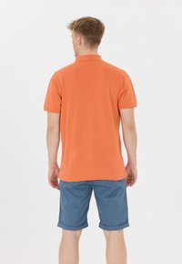 Orange polo tröja i bomull med korta ärmar och ribbad krage, kombinerad med blå uppvikta shorts för en avslappnad stil.