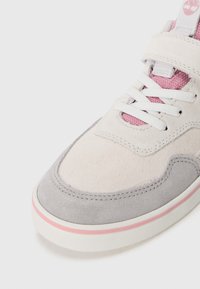 Sneaker en daim gris clair et rose avec une finition texturée, lacets blancs et un accent rose subtil sur la semelle. Présente une sangle en velcro.