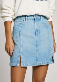 Light blue denim skirt with a straight cut, side slits, and a classic five-pocket design. Features a front button closure and belt loops.