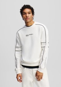 Sudadera blanca con detalles en negro, que presenta un cuello redondo, puños acanalados y "KARL LAGERFELD JEANS" bordado en el frente.