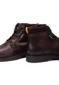 Brown leather ankle boots with a smooth finish, contrasting yellow accents at the collar, and sturdy rubber soles featuring grooves for traction.