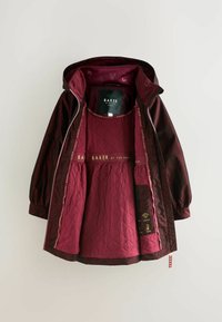 Veste matelassée bordeaux avec une couche extérieure brillante, dotée d'une capuche, d'une fermeture éclair et de détails en or sur la doublure intérieure.