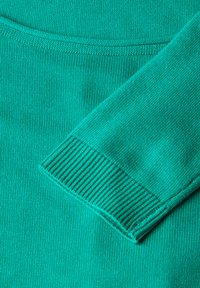 Türkiser Strickpullover mit geripptem Bündchen, glatter Textur und enger Maschen, der eine gleichmäßige Farbe und konsistente Musterung zeigt.