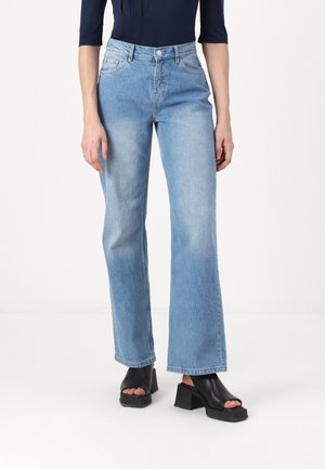 Light blue flared jeans made of denim, featuring a button closure and front pockets. Worn with black chunky heeled sandals.