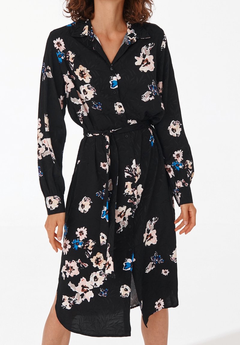 Černé květinové šaty s dlouhými rukávy, límečkem a páskem v oblasti pasu. Květinový vzor v růžových, bílých a modrých odstínech s knoflíkovými detaily.