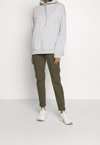 Sweat à capuche gris clair surdimensionné avec une poche kangourou, associé à un pantalon fuselé vert olive et des chaussures de sport blanches.