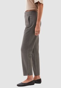 Pantalones de traje grises con corte recto, con bolsillos laterales y finas rayas. Terminan con aberturas en el dobladillo.