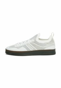 Zapatillas de punto blancas con un diseño transpirable, que presentan un upper texturizado, un cuello elástico y una suela de goma con un acento marrón.