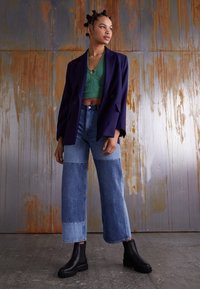 Oversized purple blazer, green cropped sweater, patchwork blue jeans, and black ankle boots. Smooth fabric with textured accents.
