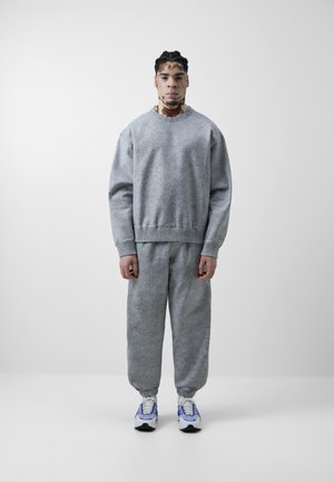 Szary, teksturowany sweatshirt i dopasowane dresy z elastycznymi mankietami. Białe sneakersy z niebieskimi i żółtymi akcentami. Prosty, luźny krój.