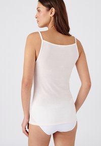 Top sin mangas de color rosa claro con tirantes finos, hecho de una tela suave. Presenta un escote redondeado y una parte posterior ligeramente más larga con aberturas laterales.