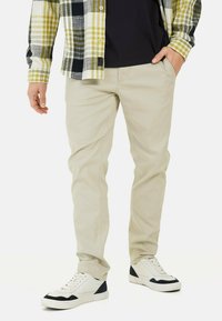 Beige slanke bukser i bomuldsstof, parret med en ternet flannel skjorte i gul og sort, samt hvide sneakers med marineblå accenter.